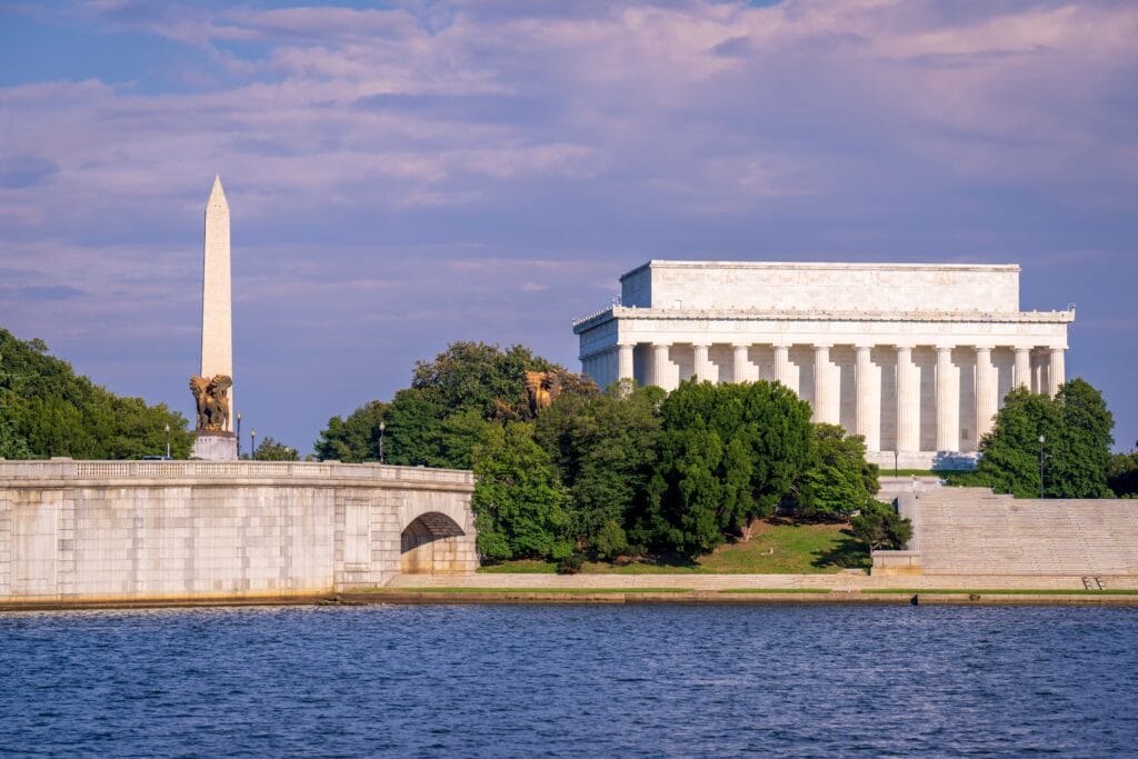 Scenic view of Lincoln Memorial and Washington Monument in DC, surrounded by lush greenery and calm waters.